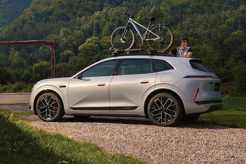 A silver Avatr 07 SUV parked on a gravel driveway with a bicycle mounted on its roof rack, seen from the side