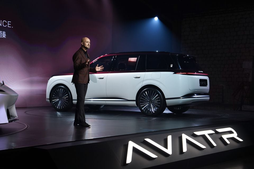 White Avatr Concept T09 SUV with a dark roof shown side-on on stage as a presenter speaks at a media launch event