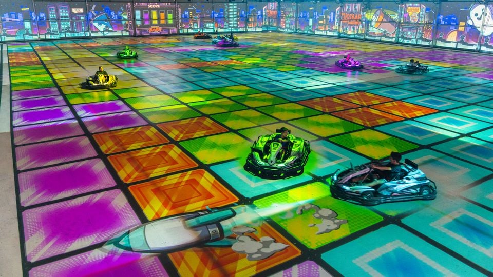 People riding electric go-karts on a colourful illuminated track with projected graphics at BattleKart Sydney