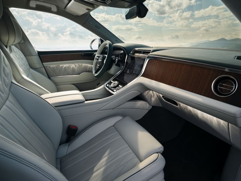 The light-coloured leather and wood interior of a Bentley, showing the dashboard, steering wheel and front seats.