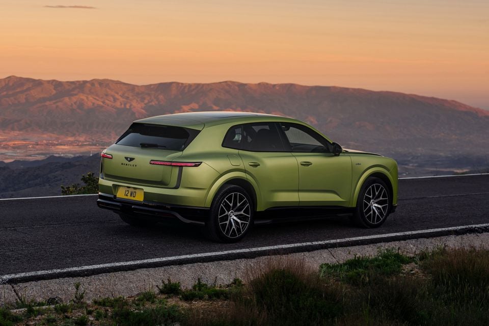 A green Bentley SUV photographed from the rear quarter on a mountain road at sunset
