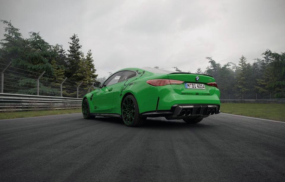 A green BMW M4 coupe seen from the rear three-quarter angle on a race track, featuring a carbon diffuser and quad exhausts, with Nurburgring 100th anniversary livery