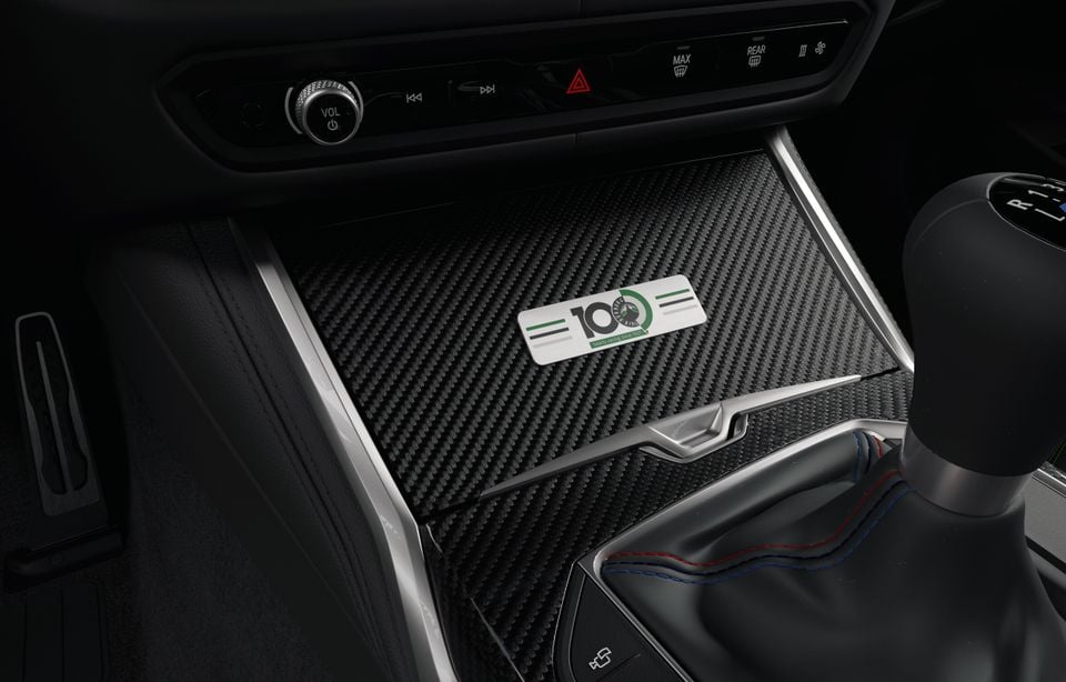 BMW car interior centre console with carbon fibre trim, a gear shifter with red and blue stitching, and a '100 Jahre Nürburgring' anniversary badge
