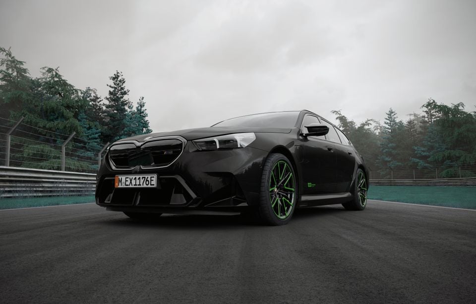 A black BMW M5 Touring wagon with green-accented wheels on a race track, part of the Nürburgring 100th anniversary edition