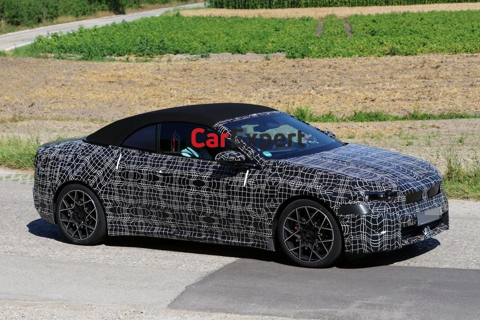 A camouflaged BMW i4 convertible prototype seen from the front-side during outdoor testing