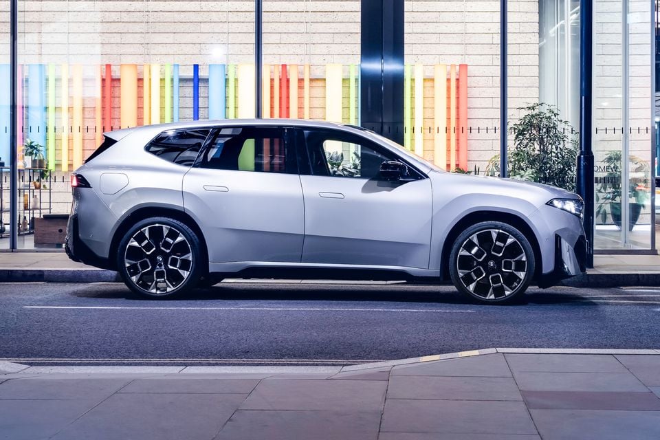 A silver BMW iX3 SUV parked on a city street, seen from the side