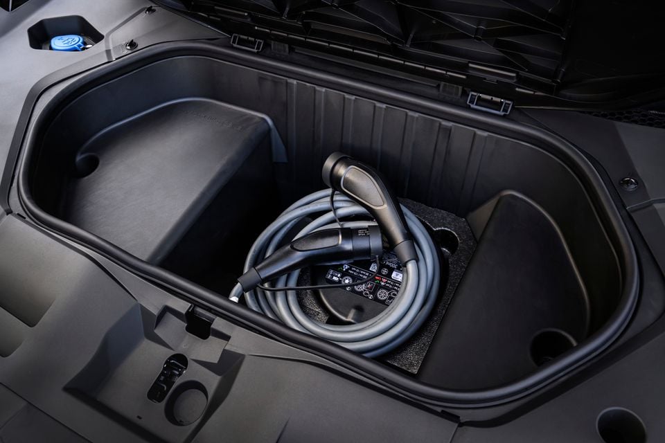 An EV charging cable coiled and stored in the front trunk (frunk) of a BMW iX3, with the bonnet open