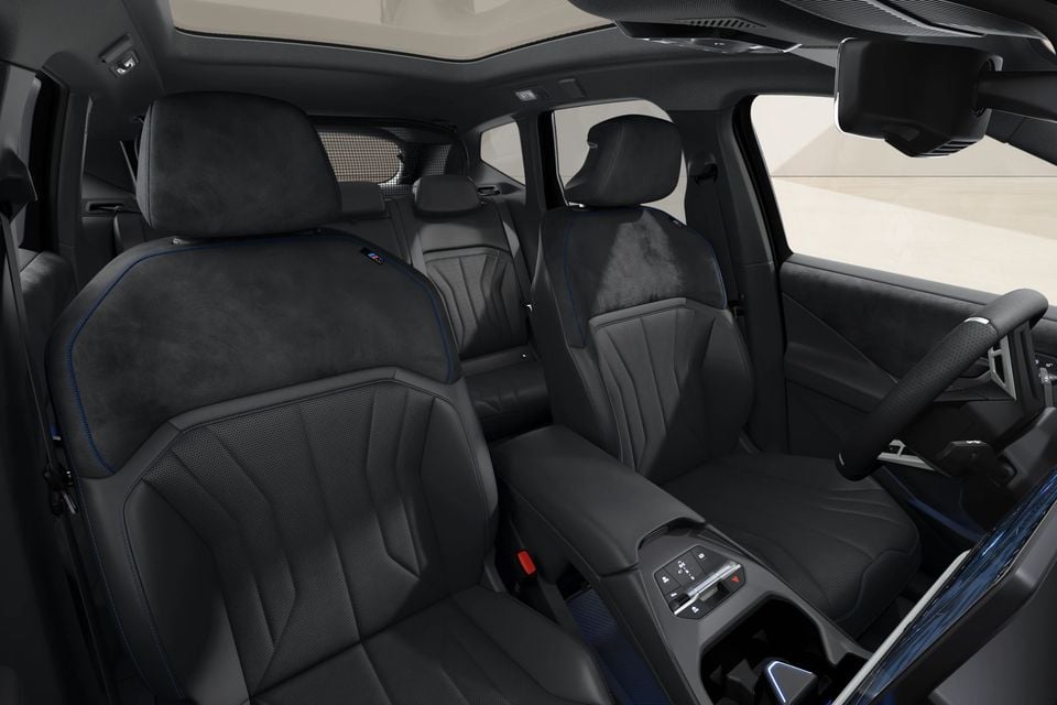 BMW iX3 interior showing dark Alcantara and leather front seats with blue contrast stitching, M badge, centre console, and steering wheel