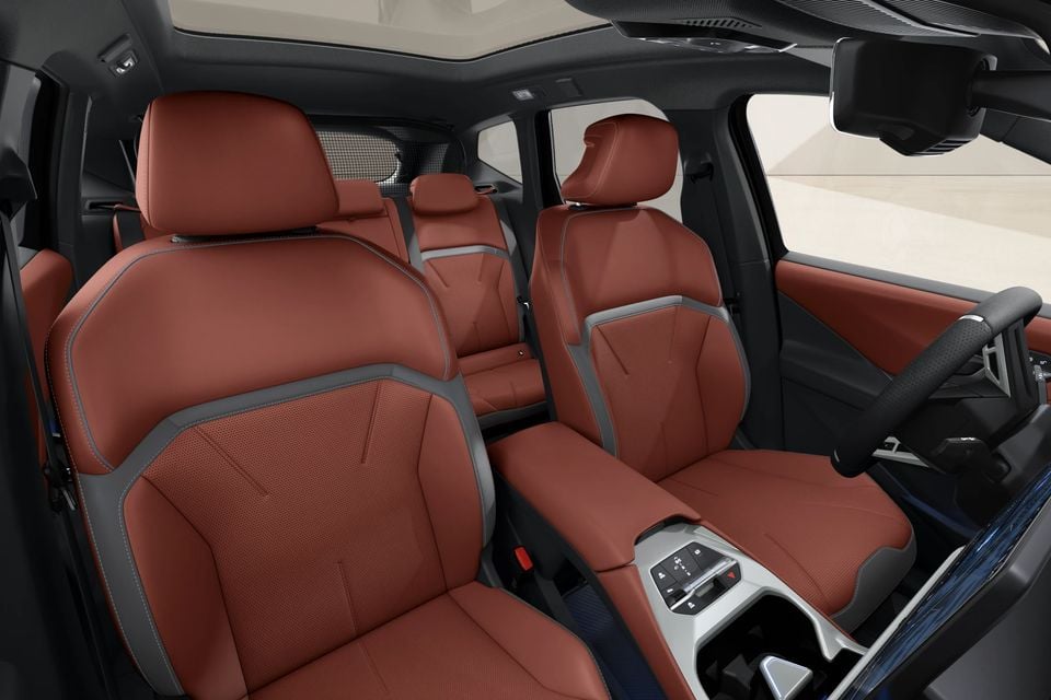 Interior of a BMW iX3 showing tan leather front and rear seats with grey contrast stitching and a centre console with controls