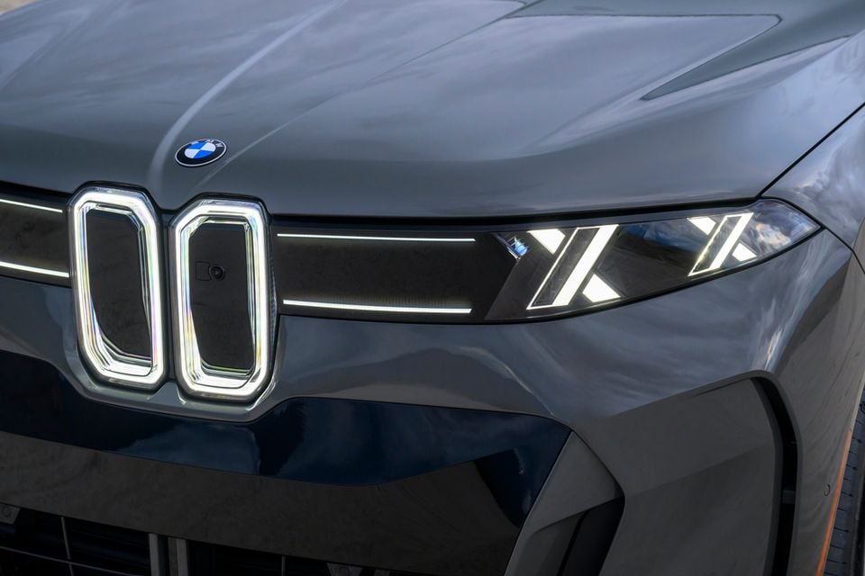 Close-up of the illuminated kidney grille and slim LED headlight on a grey BMW iX5 60 xDrive, with the BMW badge on the bonnet