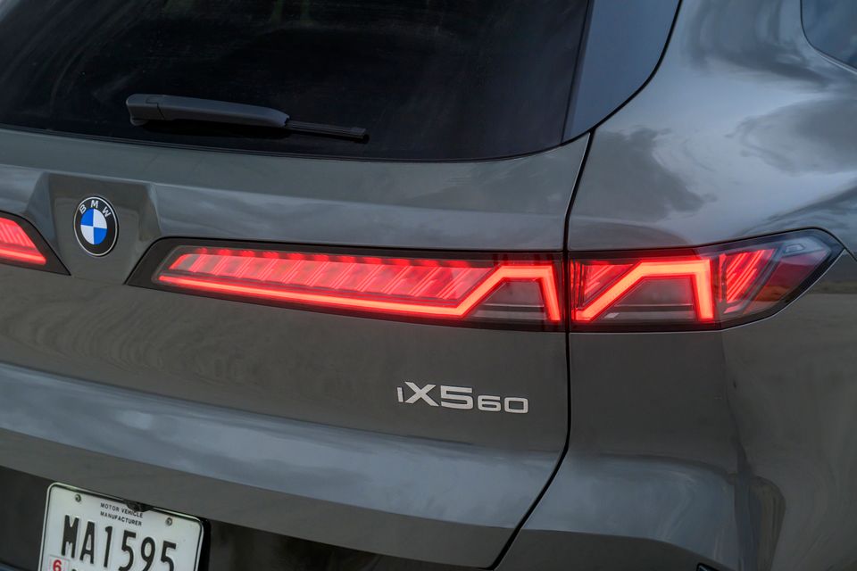 Close-up of the illuminated LED tail-light, BMW roundel and iX5 60 badge on the tailgate of a grey BMW iX5 SUV