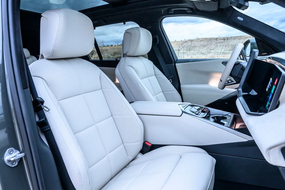 Cream leather front seats, centre console, steering wheel and touchscreen inside the BMW iX5 60 xDrive, seen through the open passenger door