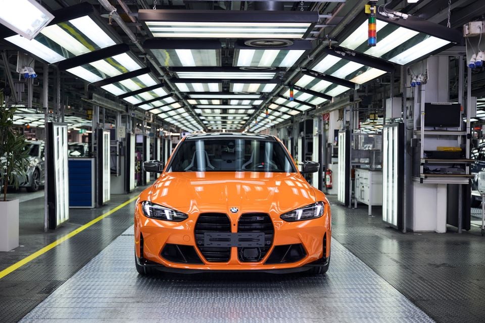 Um BMW M3 laranja visto de frente, estacionado na linha de produção dentro de uma fábrica da BMW bem iluminada