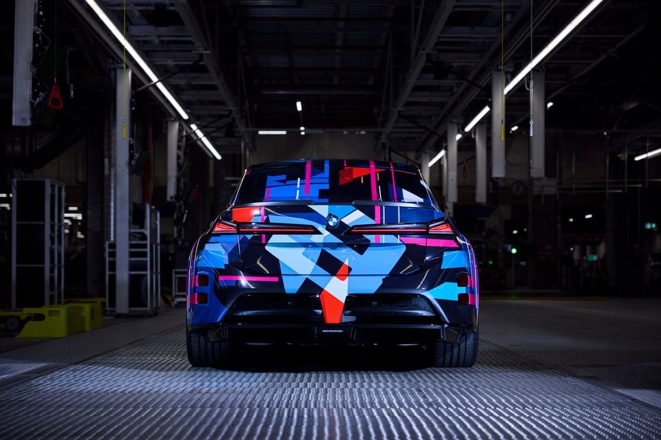 Protótipo do BMW M3 da próxima geração em camuflagem azul, vermelha e rosa, visto de trás dentro de uma fábrica
