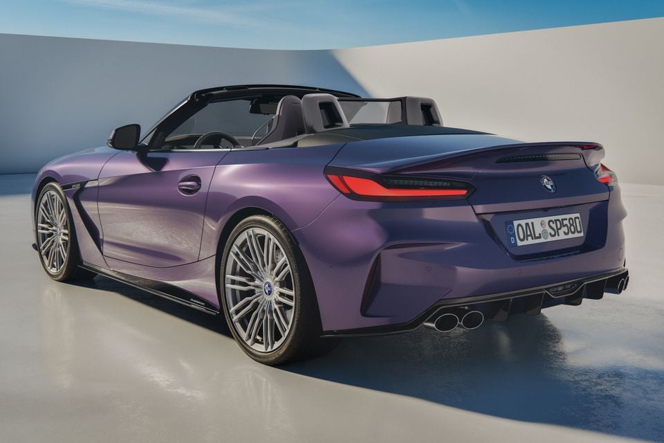 A purple Alpina Roadster convertible seen from the rear three-quarter angle, with the soft top down, featuring quad exhausts and a rear diffuser