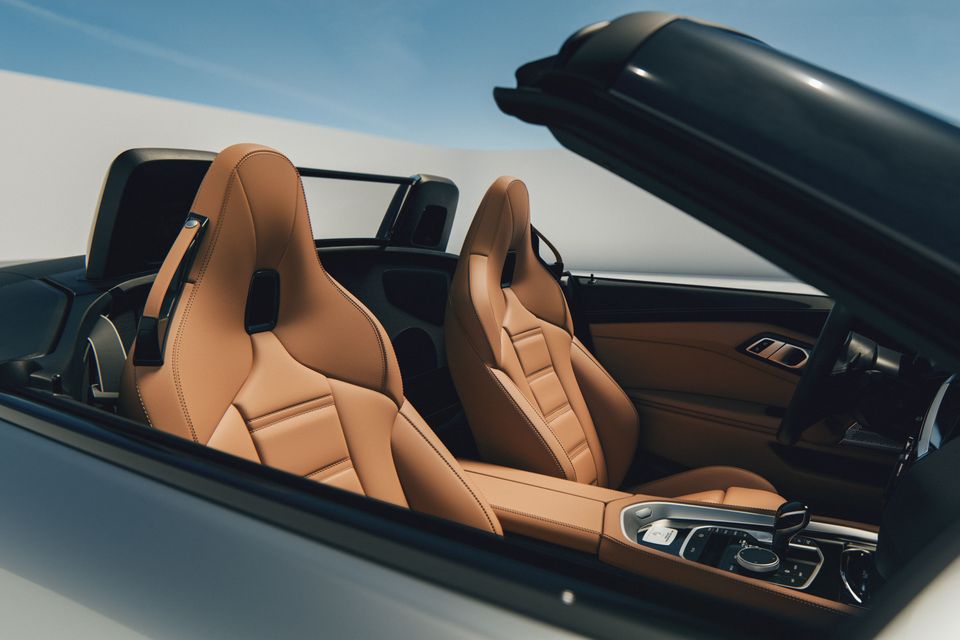 Tan leather bucket seats and centre console of a convertible sports car with the roof open, viewed from outside