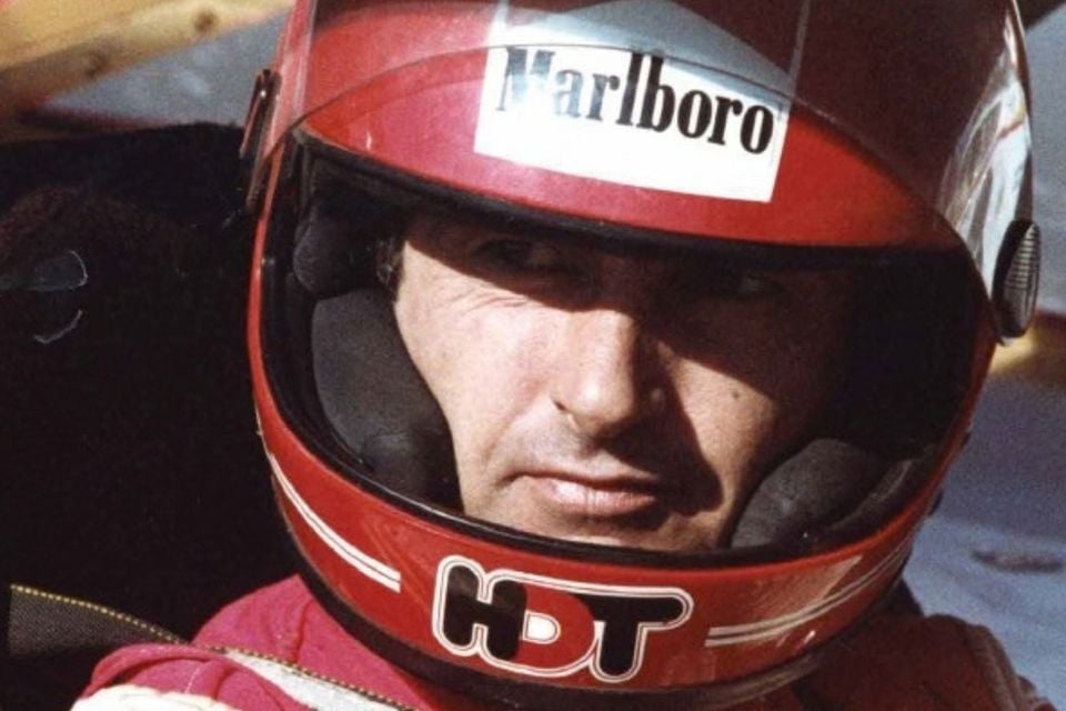Racing driver Peter Brock wearing a red full-face helmet with Marlboro and HDT logos, looking into the camera