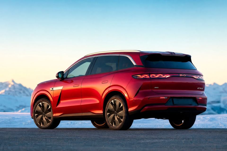 A red BYD Atto 8 SUV seen from the rear quarter, parked in front of snow-capped mountains at sunset
