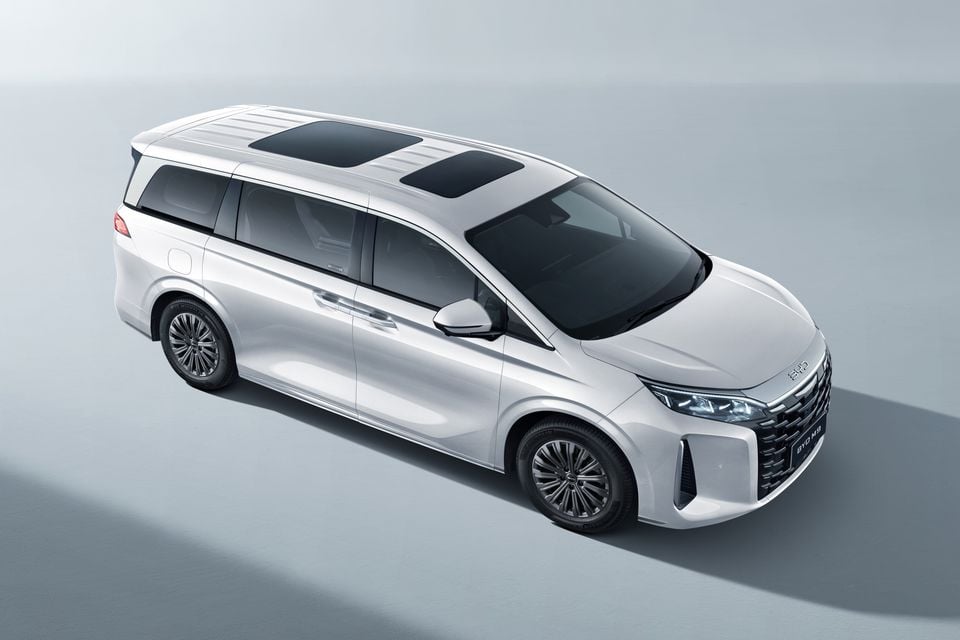 A white BYD M9 minivan seen from a high front-three-quarter angle, showing its panoramic sunroof and sliding rear doors against a studio background.