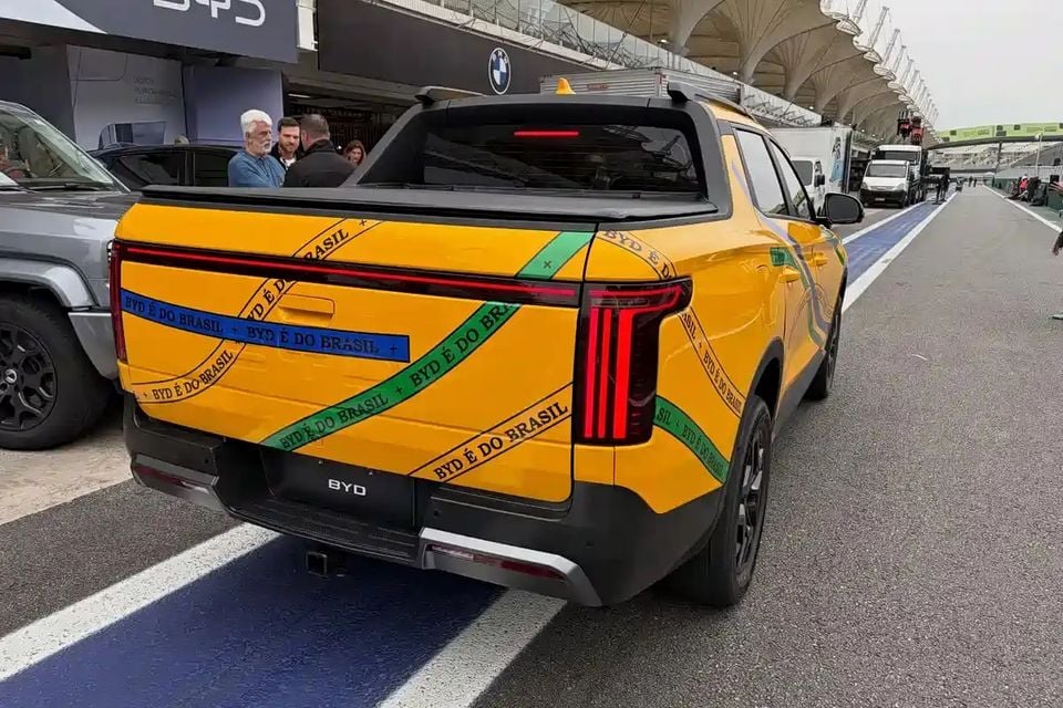 Rear view of a yellow BYD Mako ute with a Brazilian-themed 'BYD é do Brasil' wrap, pictured in a motorsport pit lane