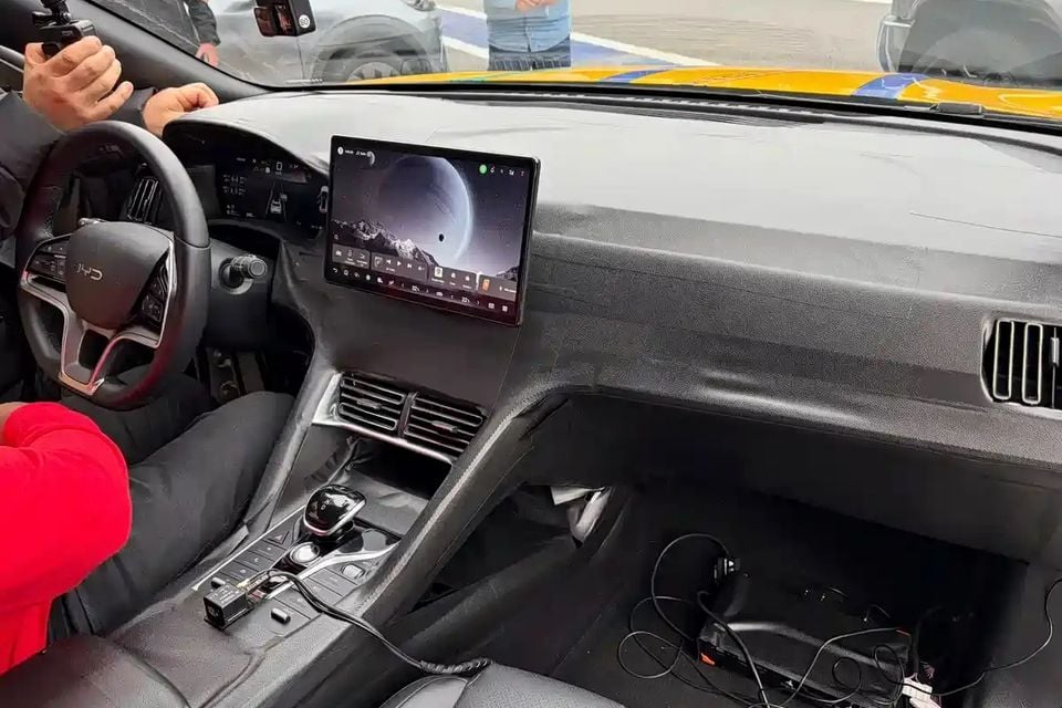 Interior of a BYD Mako showing the dashboard, central touchscreen infotainment display, steering wheel, and centre console, with cables visible on the passenger floor