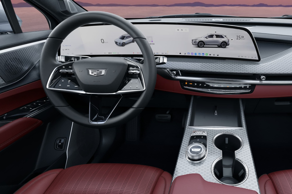 Cadillac XT5 PHEV interior showing a large panoramic dual-screen display, red leather seats, centre console with rotary dial, and a Cadillac-badged steering wheel