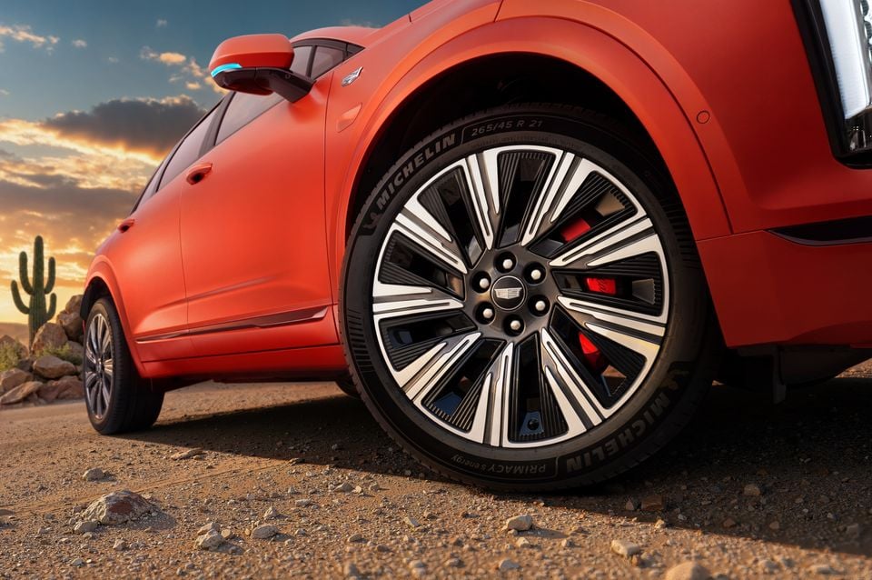 Close-up of a 21-inch Michelin Primacy S Energy tyre and multi-spoke alloy wheel on an orange Cadillac XT5 PHEV SUV, parked on a desert dirt road at sunset