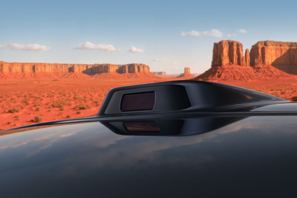 Close-up of a sensor or camera module on the roof of a dark-coloured Cadillac XT5 PHEV, with a red desert landscape in the background