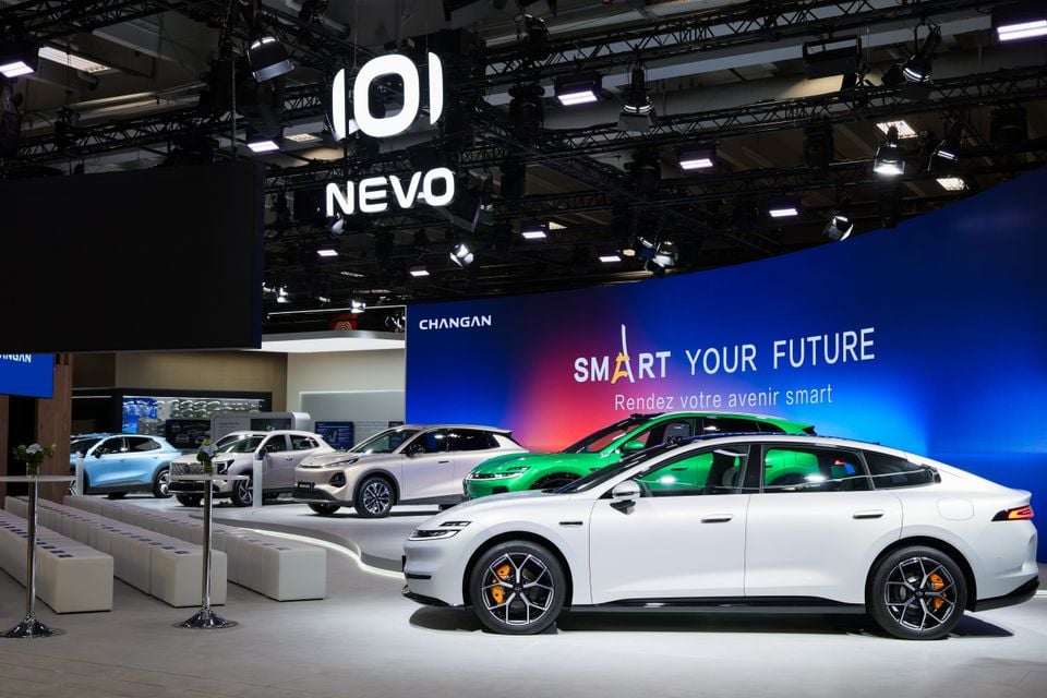 White Changan Nevo A06 sedan in profile at the Paris Motor Show, with a green sedan and Changan SUVs on display behind it