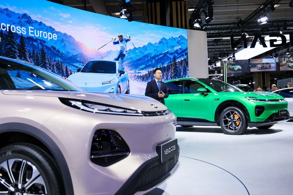 A Changan Nevo Q05 SUV and a green Changan SUV on display as a presenter speaks on the Changan stand at the Paris Motor Show