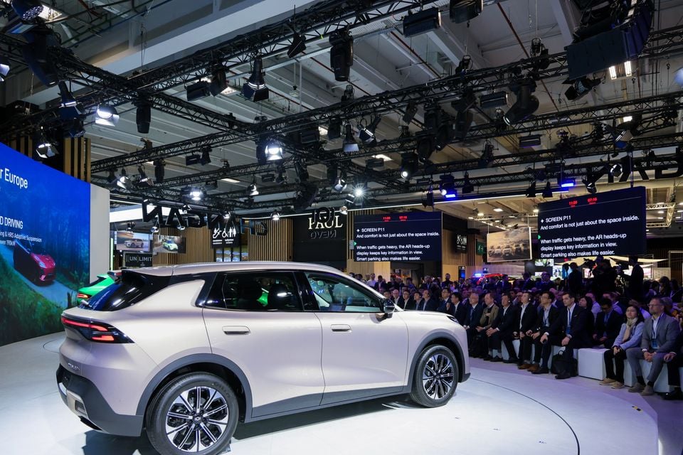 A pale silver Changan SUV seen from the rear quarter on a stage at the Paris Motor Show, with a seated audience watching a presentation