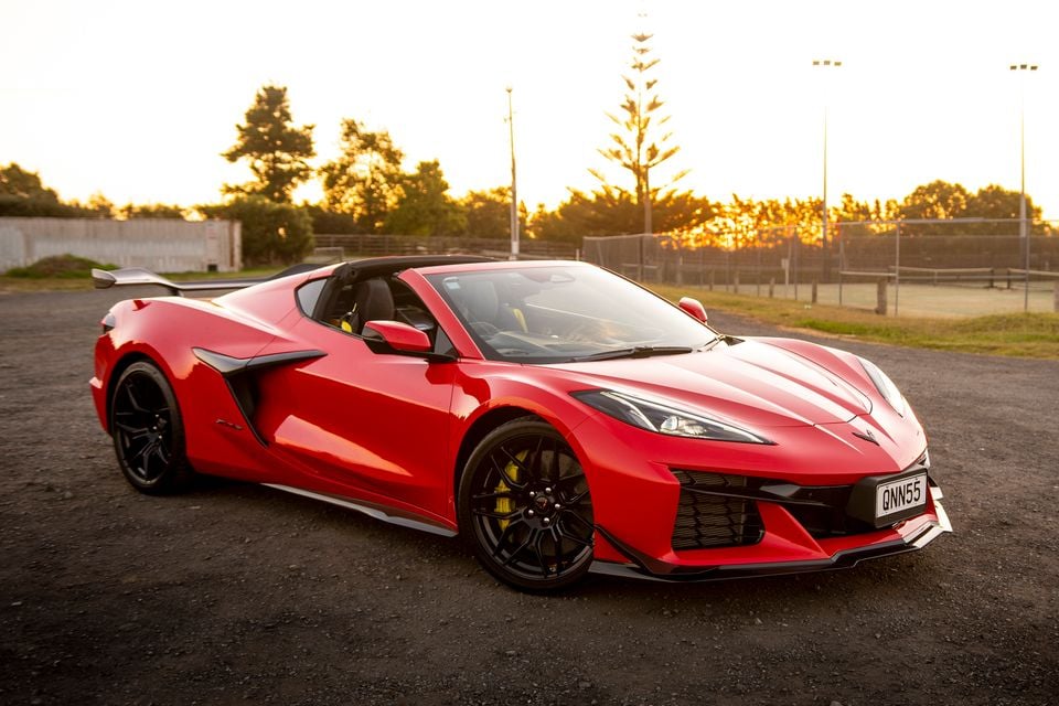 A red Chevrolet Corvette sports car seen from the front-side angle, parked on a gravel area at sunset