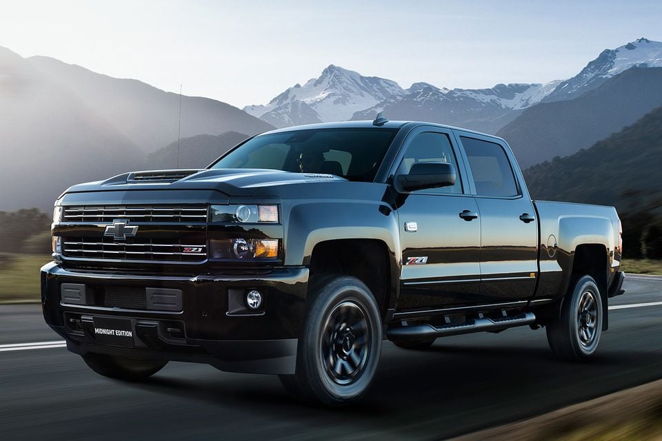 A black Chevrolet Silverado 2500 Z71 Midnight Edition crew cab pickup truck driving on a road with snow-capped mountains in the background