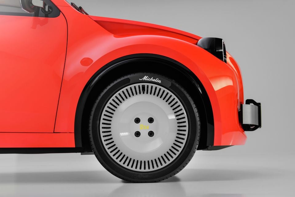 Close-up of the front wheel of a red Citroen 2CV concept, showing a white aero hubcap with a 2CV logo and a Michelin tyre