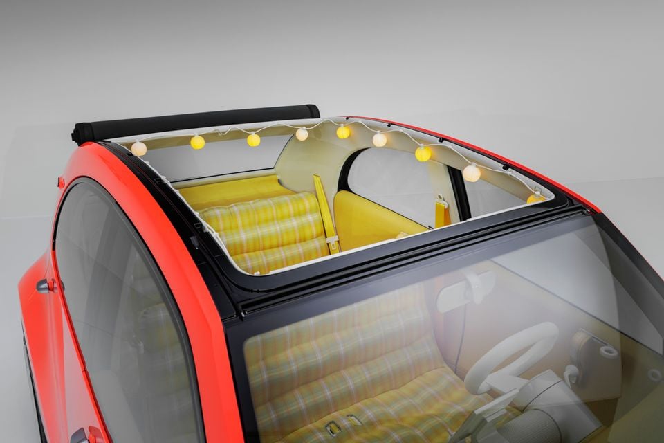 Red Citroen 2CV concept seen from above, its fabric roof rolled back to reveal yellow plaid seats and a string of paper lanterns