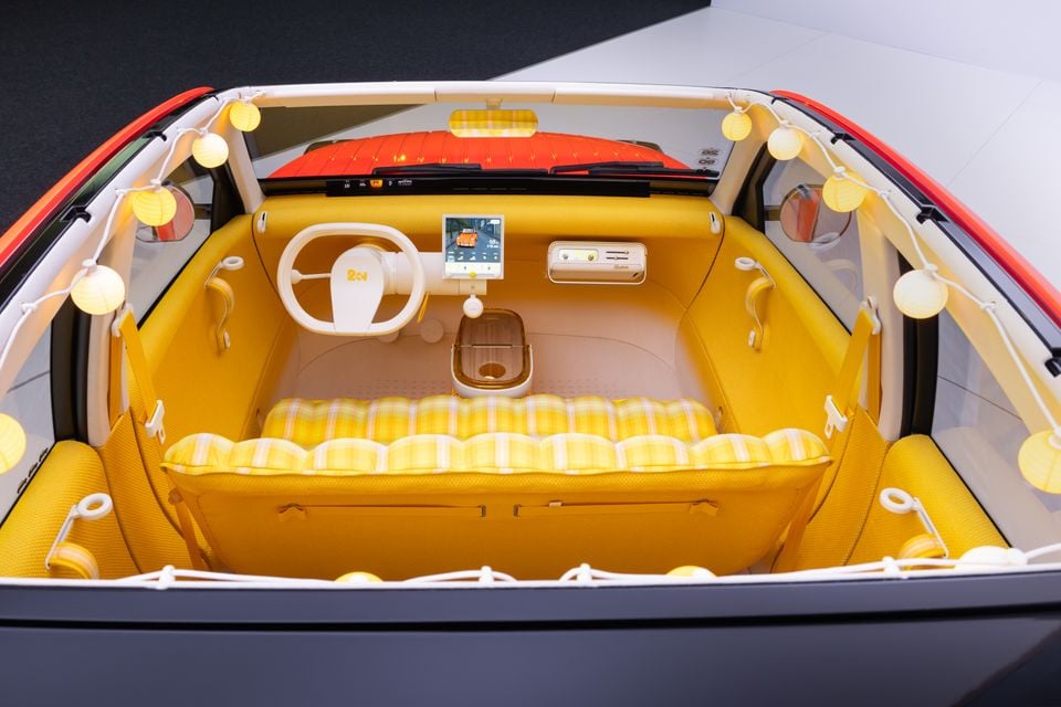 Cabin of the Citroen 2CV concept seen from above and behind, with a yellow interior, white steering wheel, small screen, checked bench seat and string lights