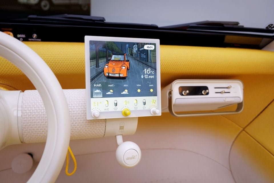 Dashboard of the Citroen 2CV concept with a cream steering wheel, small touchscreen showing a weather display, climate toggles and a yellow fabric dash