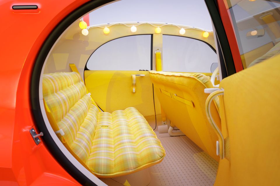 Rear cabin of the Citroen 2CV concept seen through the open orange rear door, with a yellow plaid bench seat and string lights along the roof