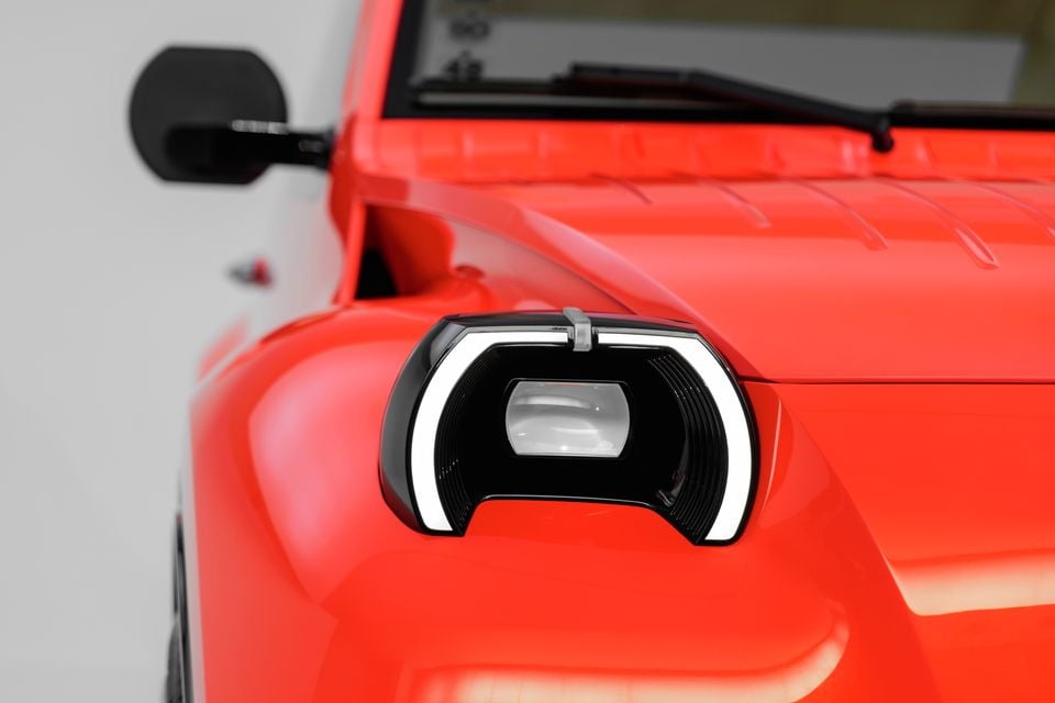 Close-up of the curved LED headlight on a bright red Citroën 2CV concept, with the ribbed bonnet and a round side mirror behind it
