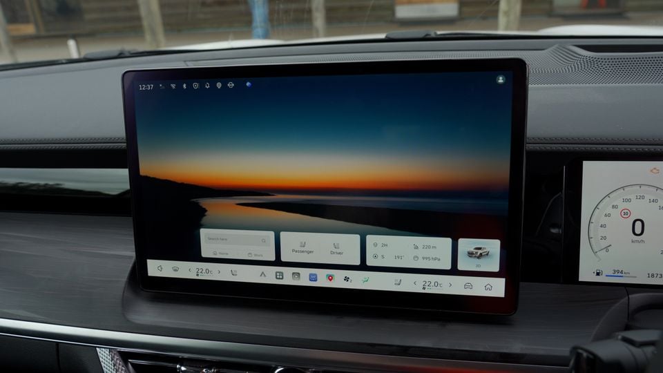 Close-up of a large touchscreen infotainment display showing a home screen with navigation, climate controls set to 22 degrees, and a digital instrument cluster visible to the right