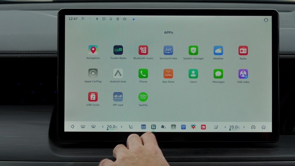 A hand pointing at a car infotainment touchscreen displaying an app menu including Navigation, Apple CarPlay, Android Auto, Spotify and other apps