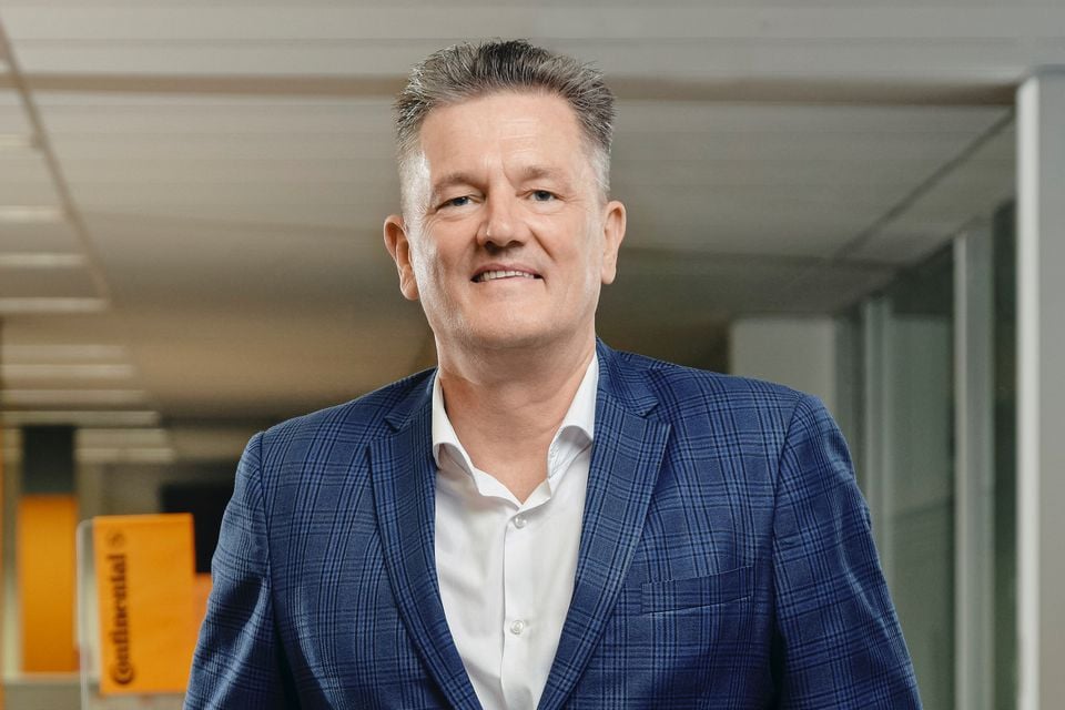 Continental managing director Mitchell Golledge smiling in a blue checked blazer and white shirt in an office with Continental signage