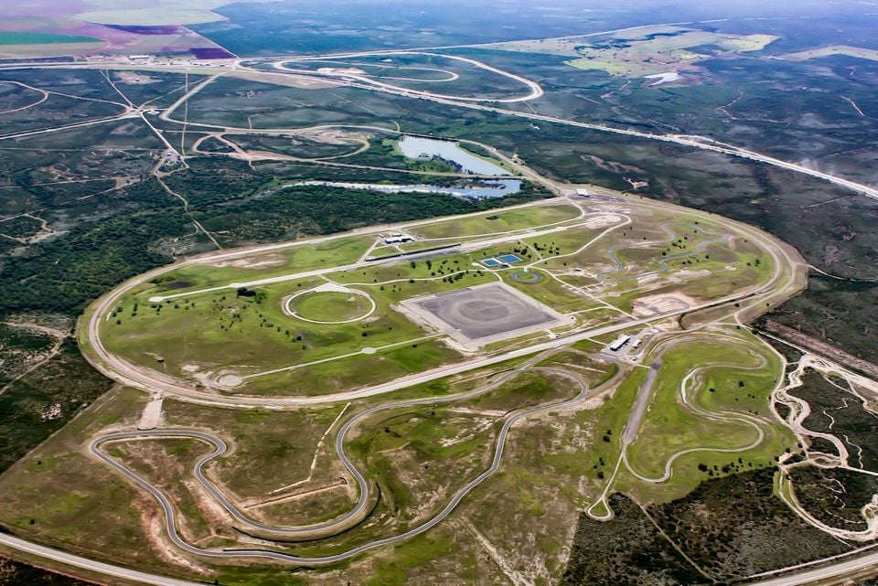 Aerial view of a large automotive proving ground with an oval track, handling circuits, skid pad, and various test roads set across open countryside.
