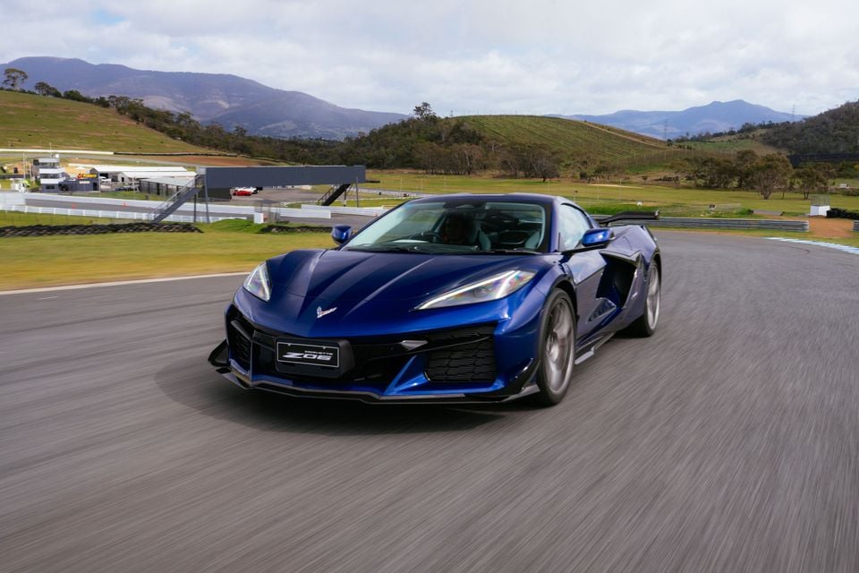 A blue Chevrolet Corvette Z06 sports car driving on a race track with mountains in the background.