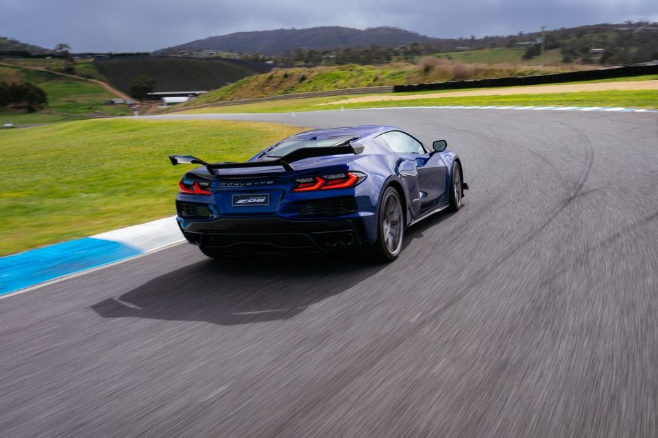 A blue Chevrolet Corvette Z06 sports car driving on a racetrack, seen from the rear quarter