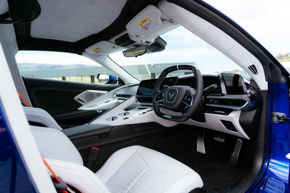 The white and black interior of a Chevrolet Corvette Z06, showing the steering wheel, dashboard and front seats through the open door.