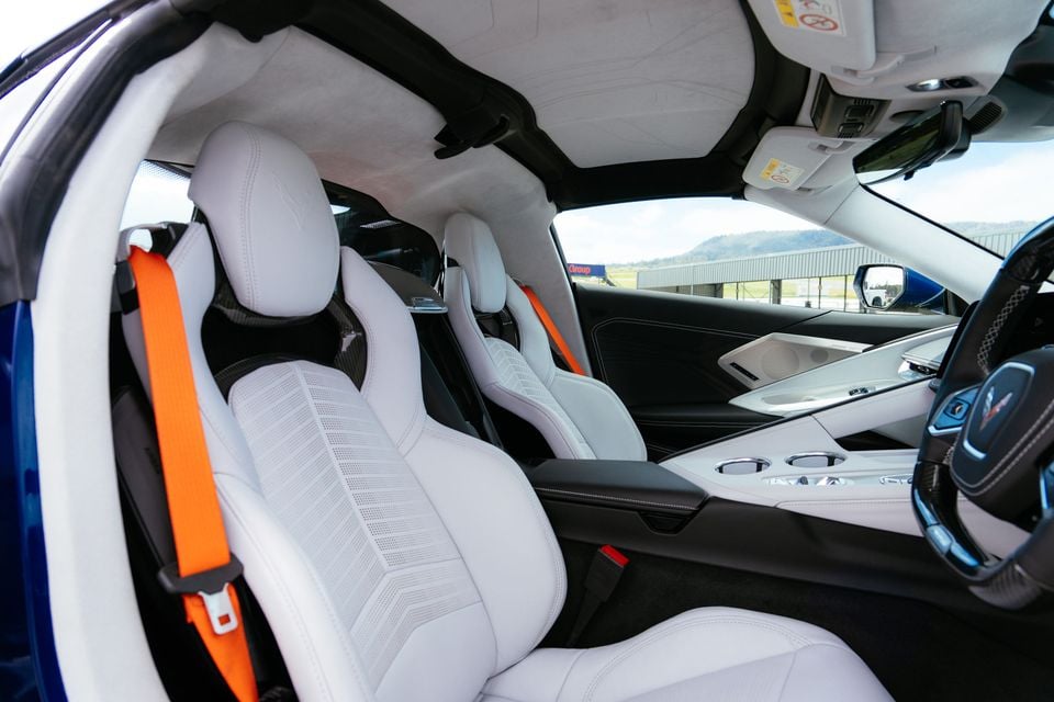 The white and black interior of a Chevrolet Corvette Z06, showing the seats, orange seatbelts, and dashboard from the passenger side
