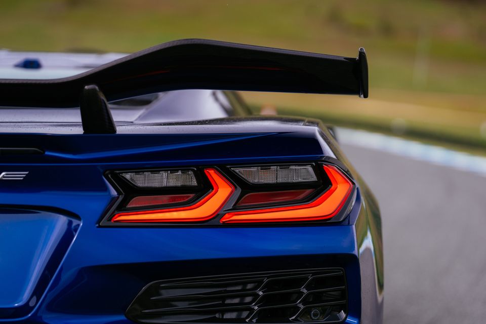 Close-up of a blue Chevrolet Corvette Z06's rear taillight and large rear wing on a racetrack