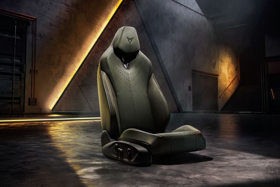 A Cupra-branded car seat with green ribbed fabric upholstery, displayed standalone in a dramatic industrial-style setting with warm ambient lighting