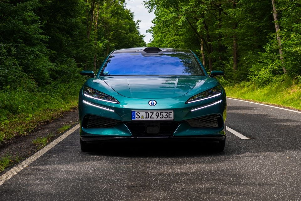 A teal Denza Z9 GT seen from the front, stopped on a tree-lined road